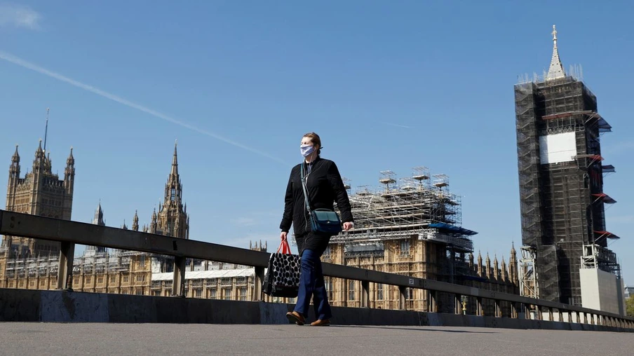 Uma mulher usando uma máscara facial atravessa a ponte de Westminster com o relógio Big Ben e as Casas do Parlamento em segundo plano, enquanto a disseminação da doença por coronavírus