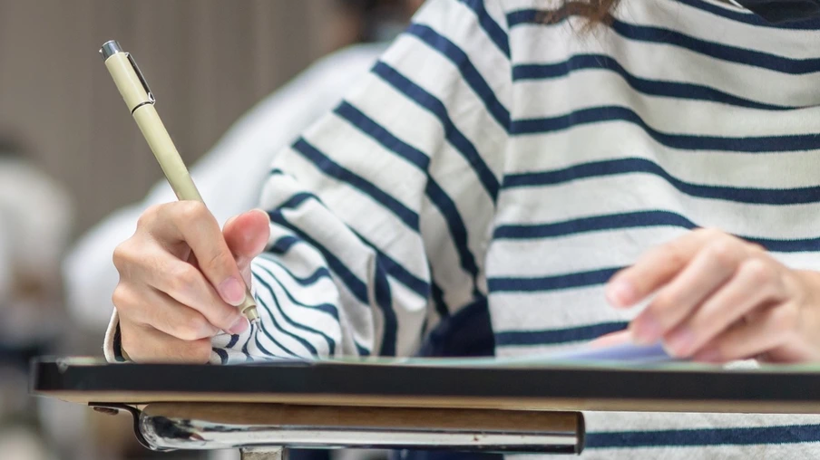 Exam at school with student's taking educational admission test in class, thinking hard, writing answer in university classroom, education and world literacy day concept