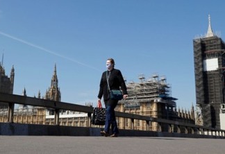 Uma mulher usando uma máscara facial atravessa a ponte de Westminster com o relógio Big Ben e as Casas do Parlamento em segundo plano, enquanto a disseminação da doença por coronavírus