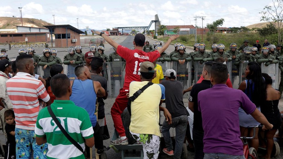 Pessoas esperando para atravessar para a Venezuela em frente aos guardas nacionais venezuelanos na fronteira entre a Venezuela e o Brasil em Pacaraima.