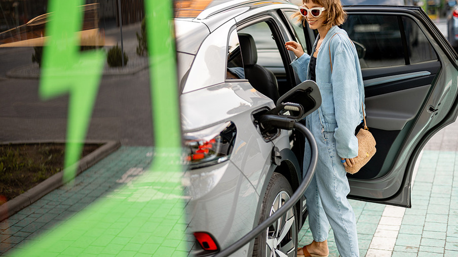 Young woman opens vehicle door of her electric car, charging it on a public charging station